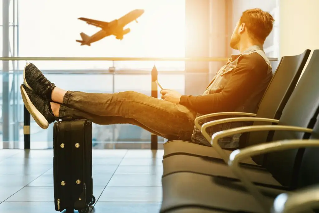man sitting on gang chair with feet on luggage looking at airplane abroad  dream